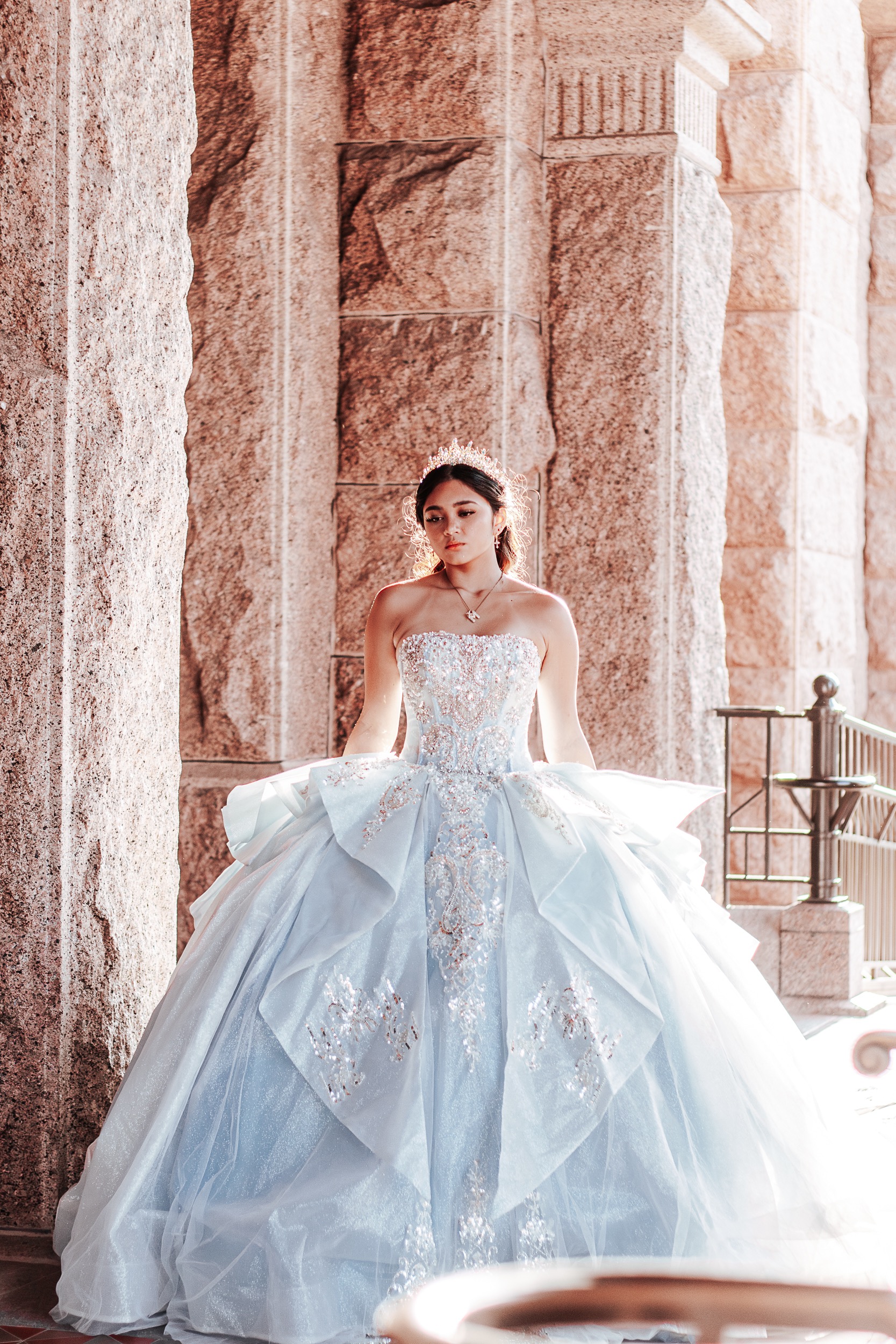 Quinceañera honoree in romantic ice-blue gown framed by warm stone columns — Austin quinceañera photographer