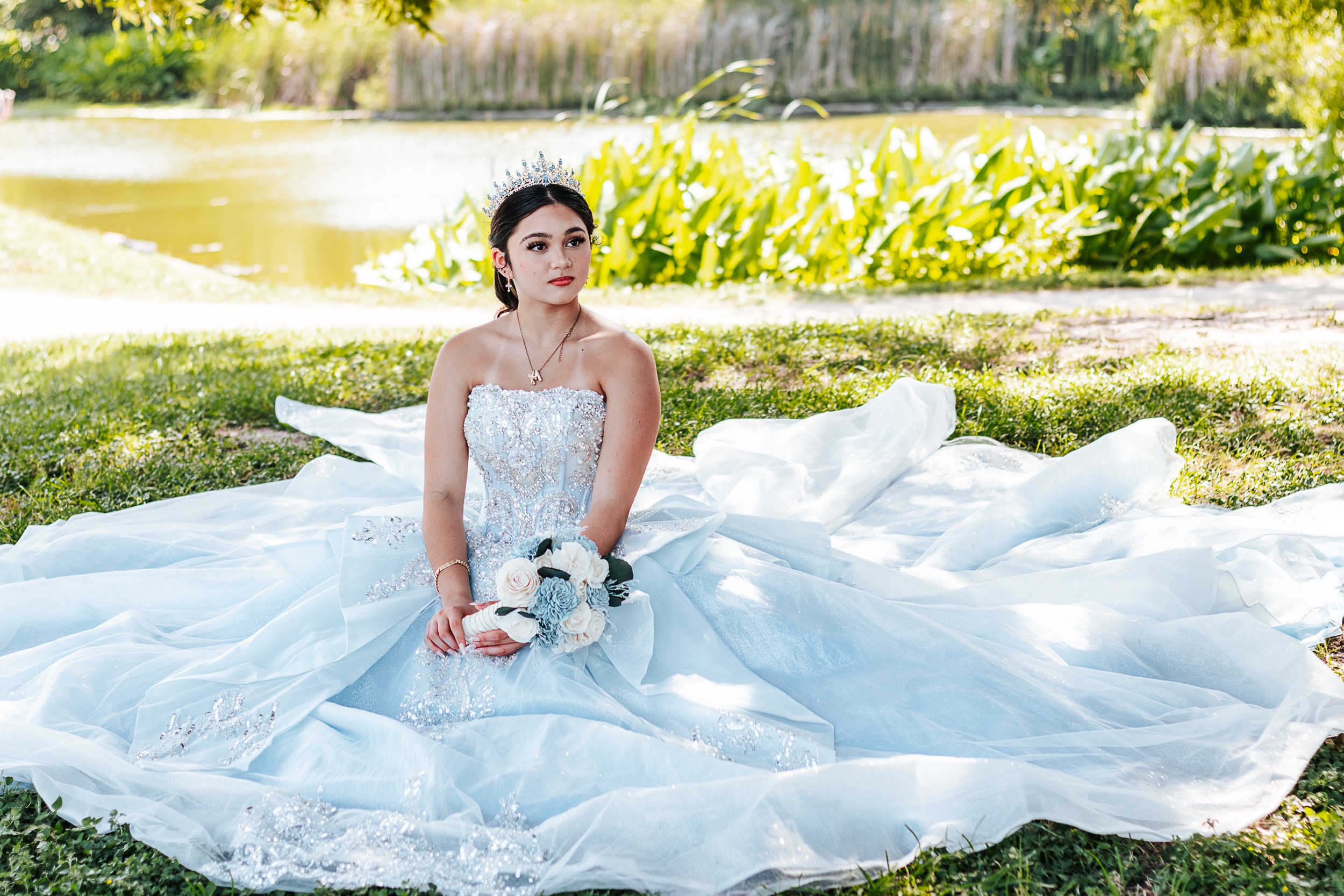 Quinceañera honoree in ice-blue ball gown seated by a pond — Austin quinceañera photography