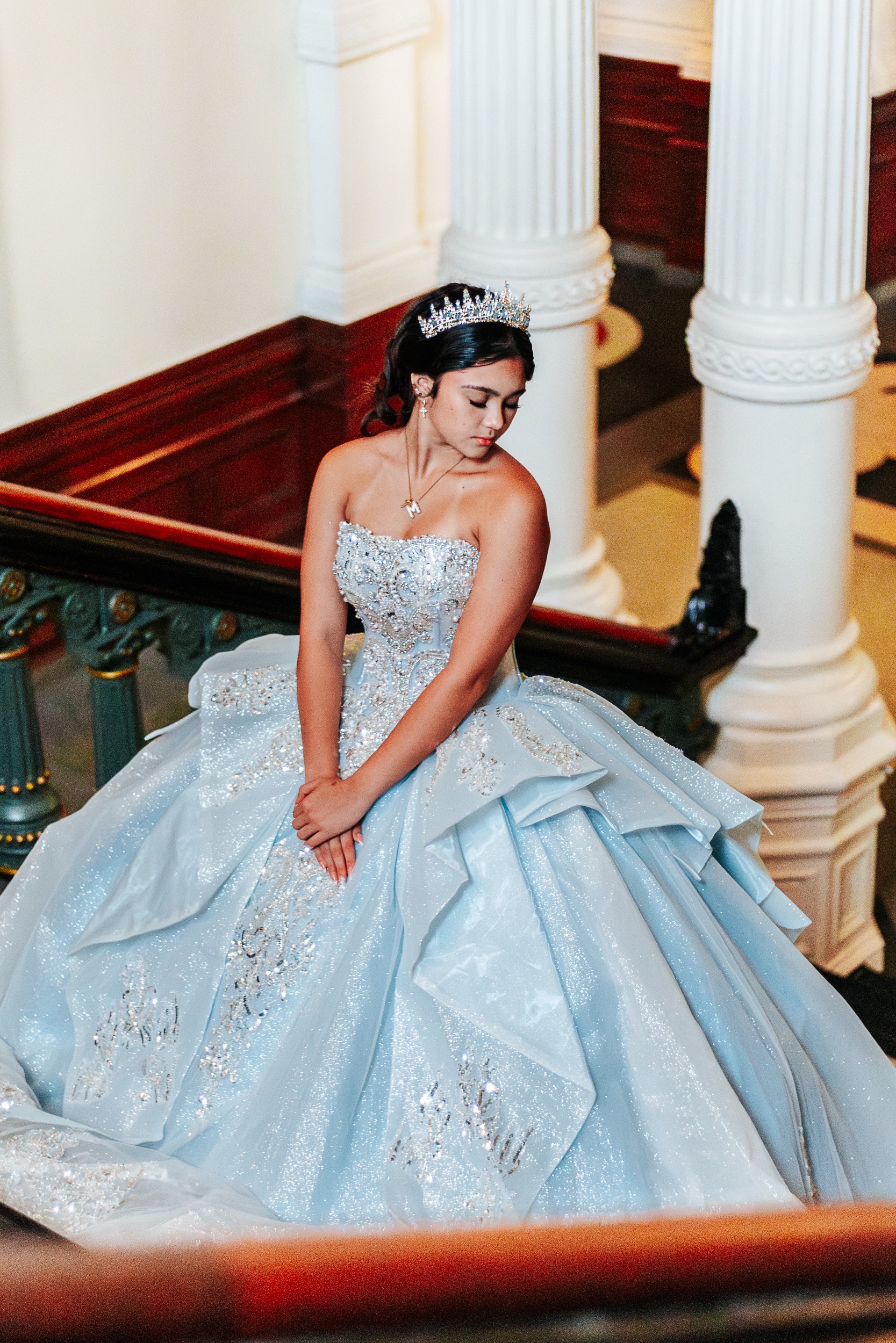 Quinceañera honoree in beaded silver and blue gown on ornate staircase — San Antonio quinceañera photography
