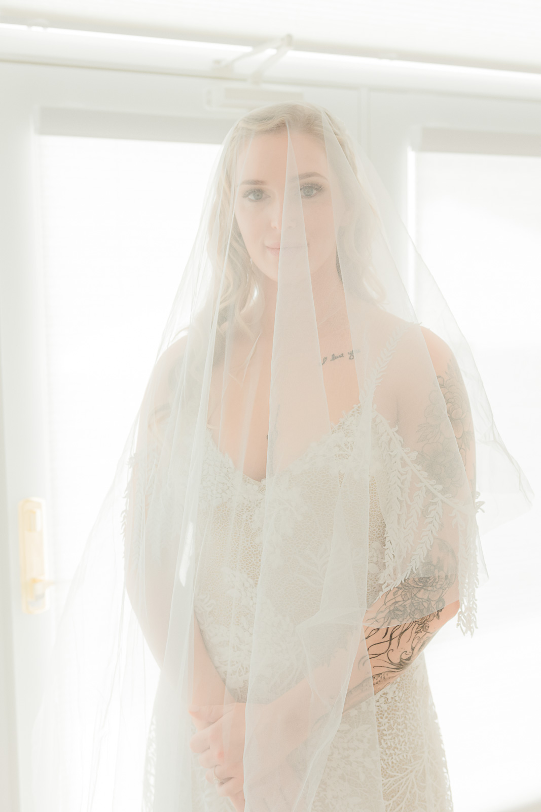 Bride in lace gown with flowing veil lit by soft window light — Texas Hill Country bridal portrait