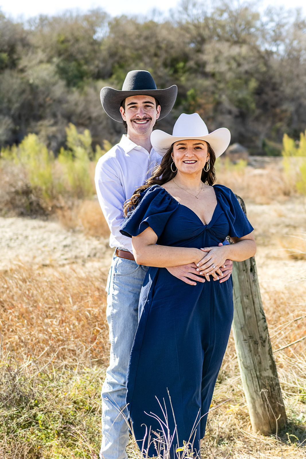 Engaged couple in cowboy hats embrace in a golden Texas Hill Country field — engagement session near Austin