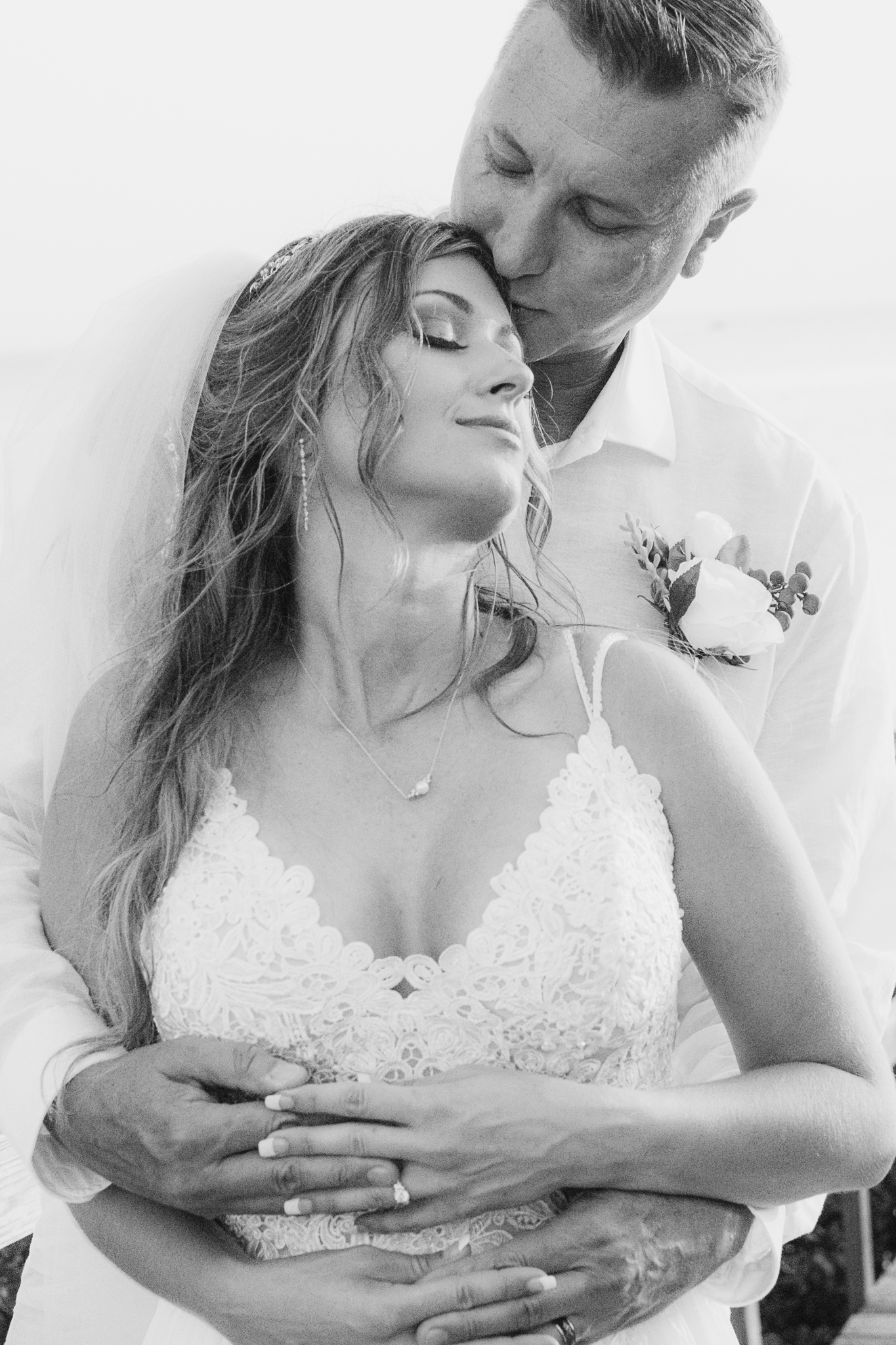 Groom holds bride from behind and kisses her temple — intimate black and white editorial wedding portrait, Texas Hill Country